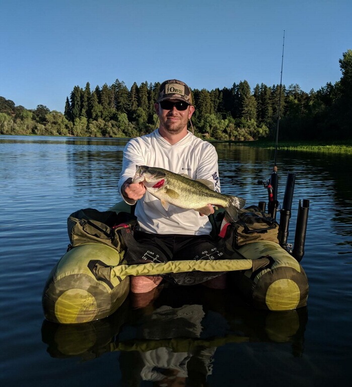 a float tube fisherman on a pond, holding a bass